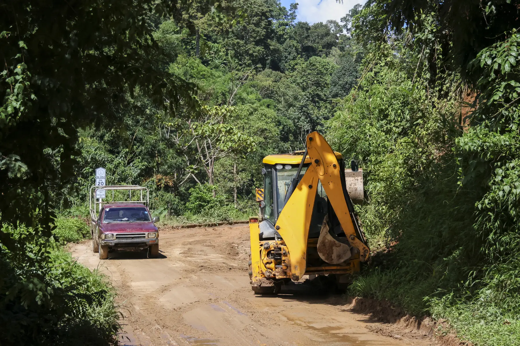 Retrocargadora trabajando en una vía rural rodeada de vegetación